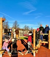 Sponsoren und Kinder vor und auf dem inklusiven Spielgerät